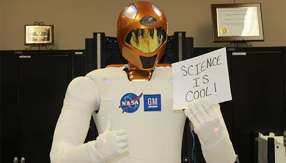 Robonaut 2 gives a thumbs-up while holding a sign that says "Science Is Cool!"
