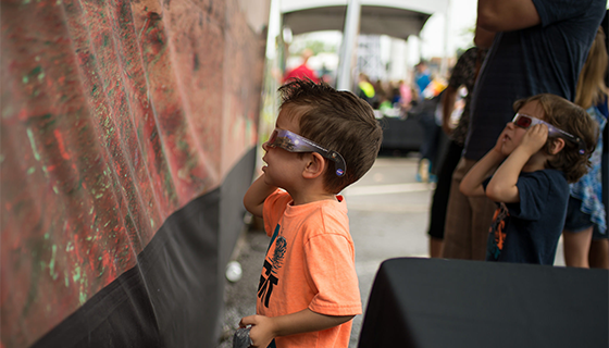 Two small children wear 3-D glasses while looking at a large banner of the surface of Mars