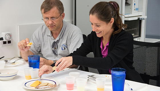 Two astronauts try crackers with cheese spread