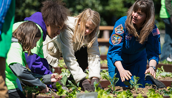 Astronaut Cady Coleman and NASA Deputy Administrator Dava Newman help two students plant lettuce in a garden