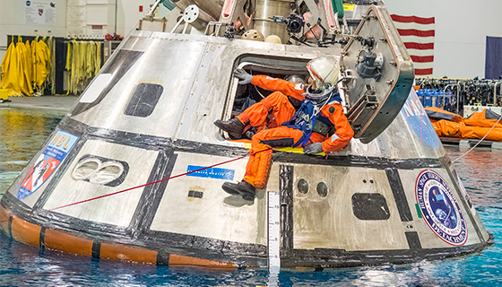 Astronaut Suni Williams exits through a door of an Orion capsule floating in a large pool
