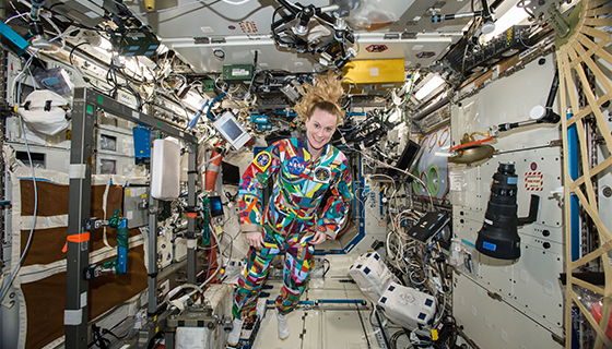 Astronaut Kate Rubins wears a multicolored flight suit while floating inside the space station