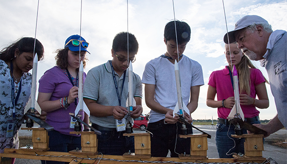 Five students place model rockets on a launch pad