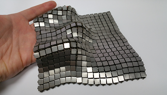 A fabric made of woven metallic squares drapes over a person's hand