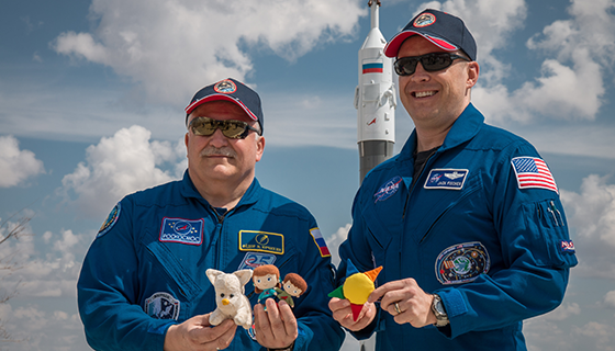 Fyodor Yurchikhin and Jack Fischer hold small stuffed toys while posing in front of a Soyuz rocket