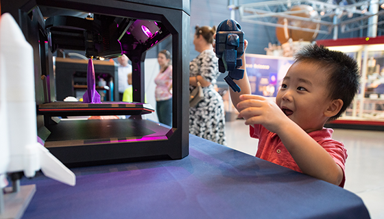A boy smiles while holding a robot figurine made by a 3-D printer