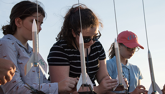 Three girls prepare model rockets for launch