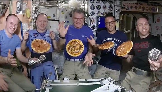 Astronauts pose with floating pizzas on the space station