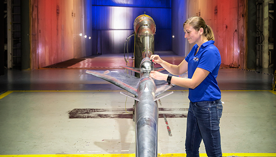 A female engineer and a silver airplane model inside a wind tunnel