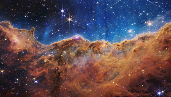 Reddish brown dust resembling mountains and valleys is speckled with bright blue and white stars