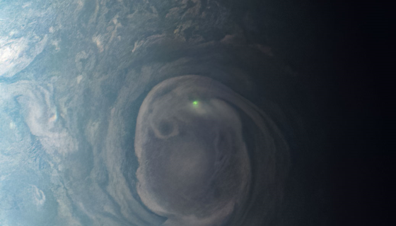 A bright green glowing dot is seen in a swirl of clouds on Jupiter