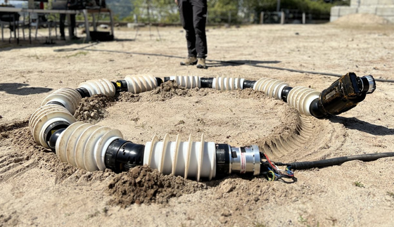 An engineer watches as a snake-like robot moves in a circle through sandy terrain