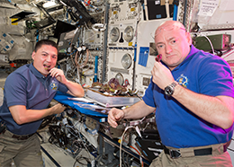 Astronauts Kjell Lindgren and Scott Kelly hold lettuce leaves grown on the space station