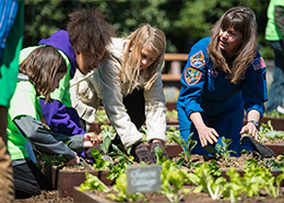 Astronaut Cady Coleman and NASA Deputy Administrator Dava Newman help two students plant lettuce in a garden