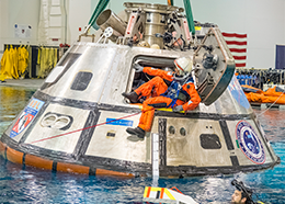 Astronaut Suni Williams exits through a door of an Orion capsule floating in a large pool