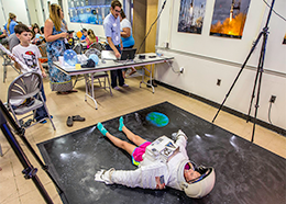 For a photo, a young girl wearing the upper part of a spacesuit lies on a large picture of space