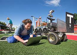 Erica Tiberia types on a laptop computer next to a robotic rover