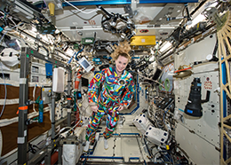 Astronaut Kate Rubins wears a multicolored flight suit while floating inside the space station