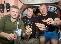 Andrey Borisenko, Shane Kimbrough and Oleg Novitskiy hold crackers topped with cheese and meat