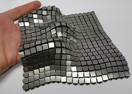 A fabric made of woven metallic squares drapes over a person's hand