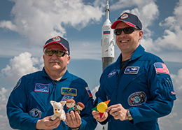 Fyodor Yurchikhin and Jack Fischer hold small stuffed toys while posing in front of a Soyuz rocket