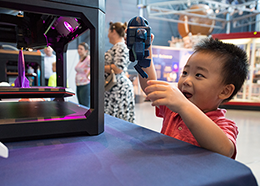 A boy smiles while holding a robot figurine made by a 3-D printer
