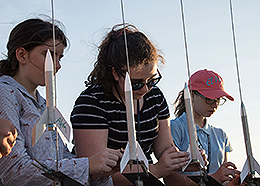 Three girls prepare model rockets for launch