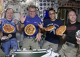 Astronauts pose with floating pizzas on the space station