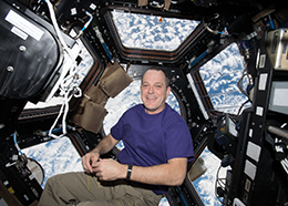 Ricky Arnold floats in front of the many windows of the space station cupola