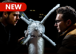 Two men closely inspect a propeller that is covered in ice crystals