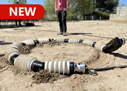 An engineer watches as a snake-like robot moves in a circle through sandy terrain