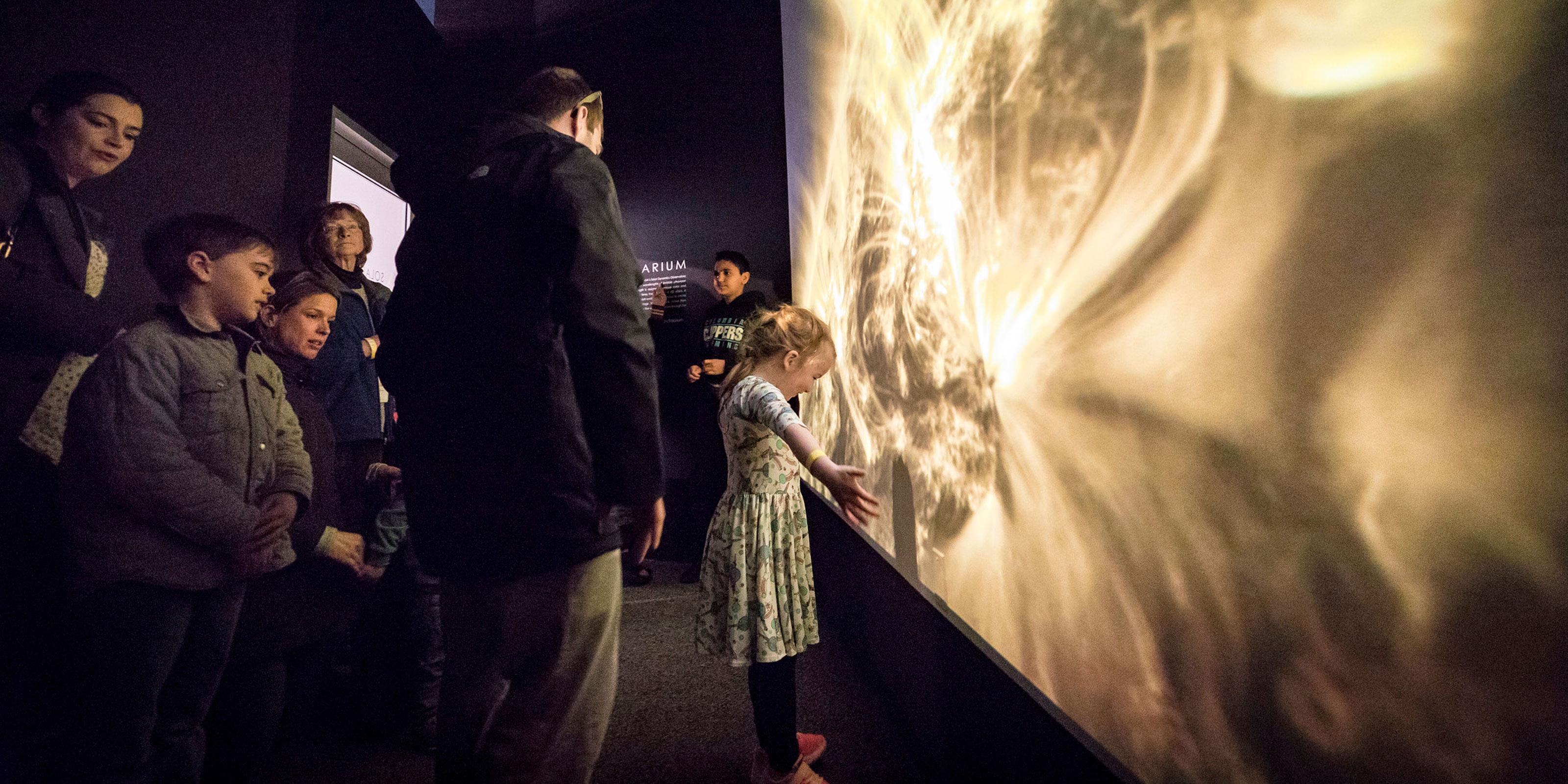 A child spreads their arms in front of a large screen.