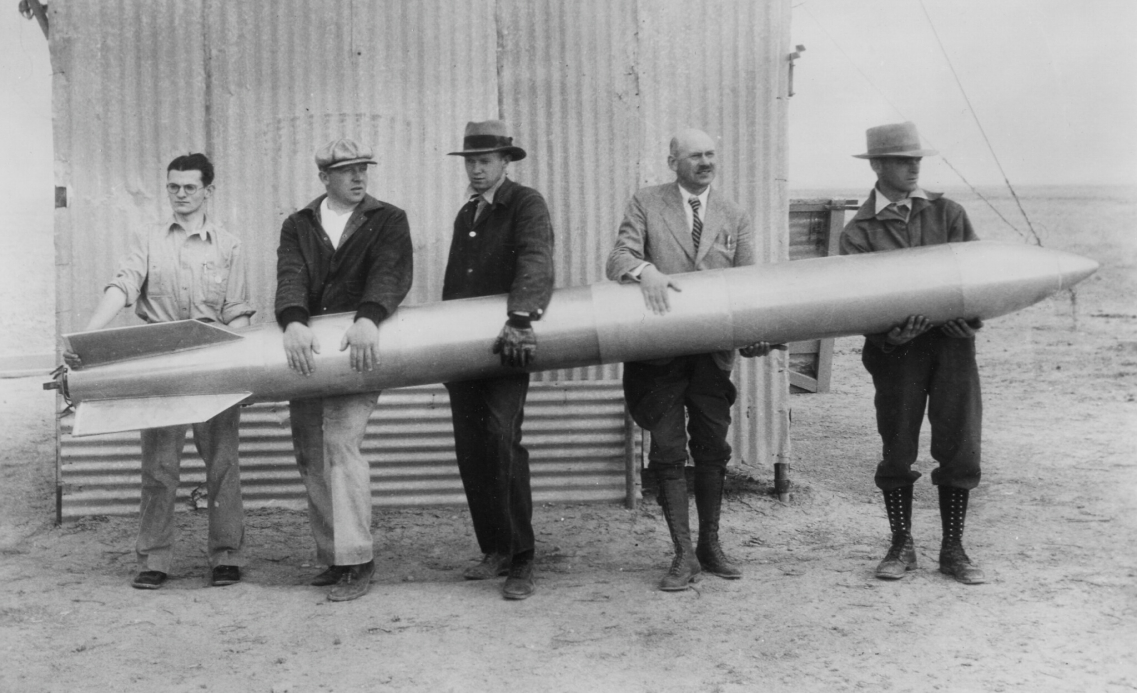 Black and white image of Dr. Robert Goddard and other colleagues all holding a large rocket.