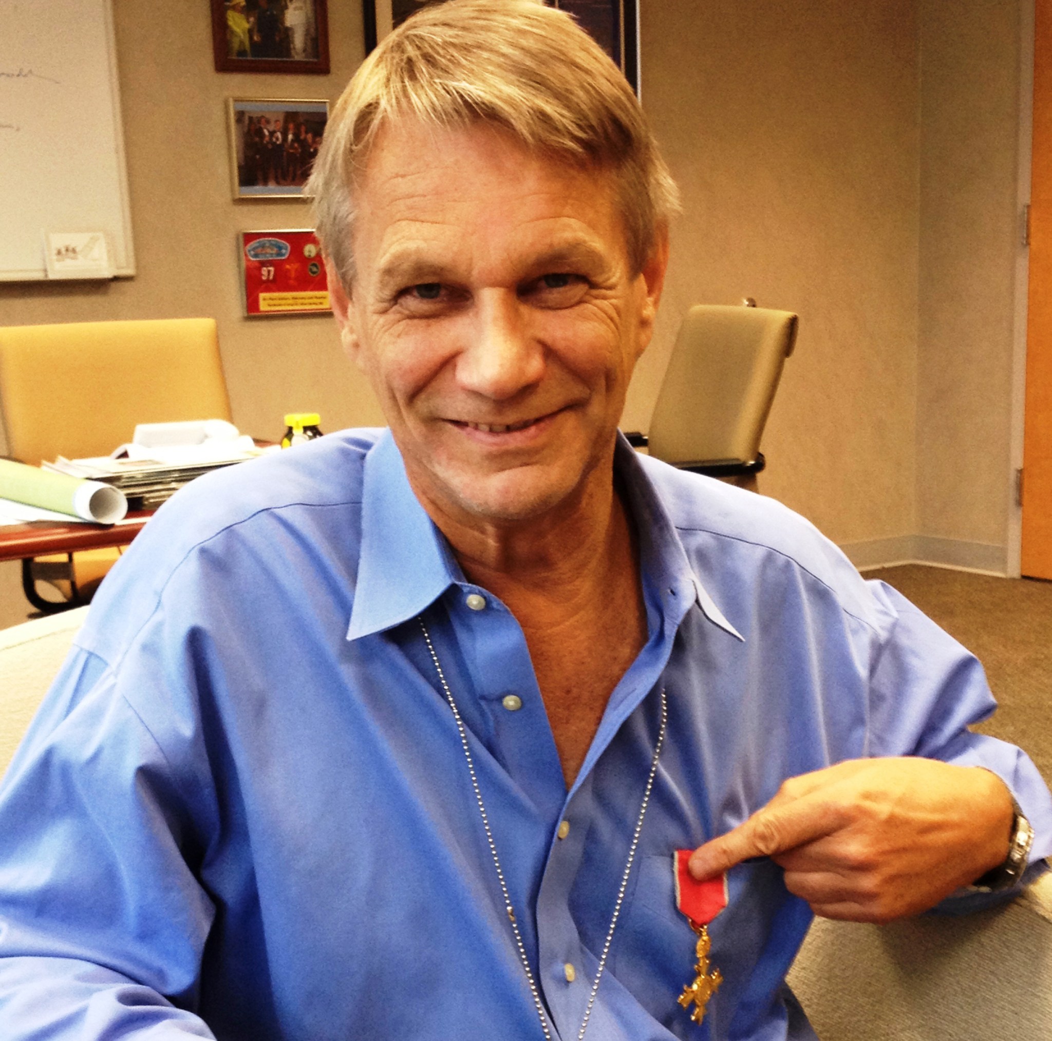 portrait of a smiling Piers Sellers pointing to a gold medal with red ribbon pinned to his shirt