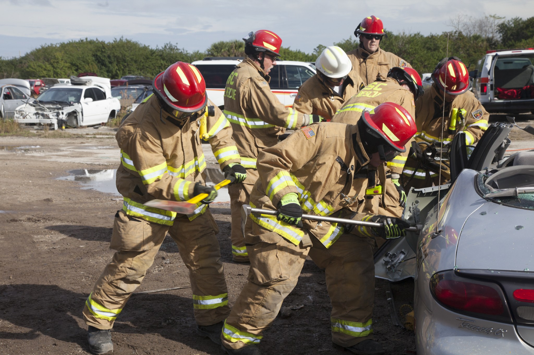 Special Rescue Operations firefighters with NASA Fire Rescue Services in the Protective Services Office at Kennedy Space Center in Florida practice vehicle extrication training at an auto salvage yard near the center. A firefighter with an axe assists as another firefighter uses a special tool to punch through the door of the vehicle.