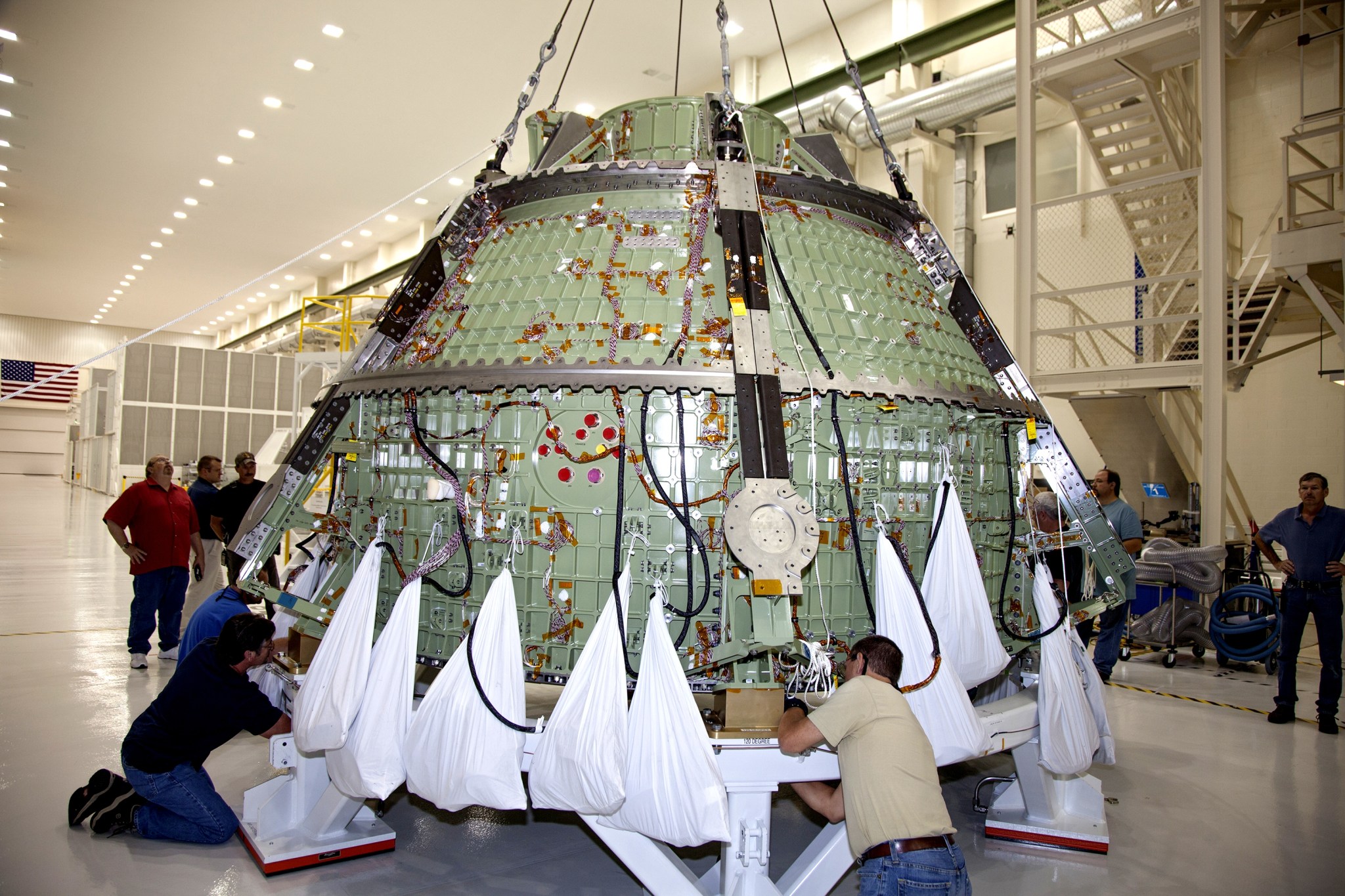 Technicians help secure the Orion crew module onto a work stand.