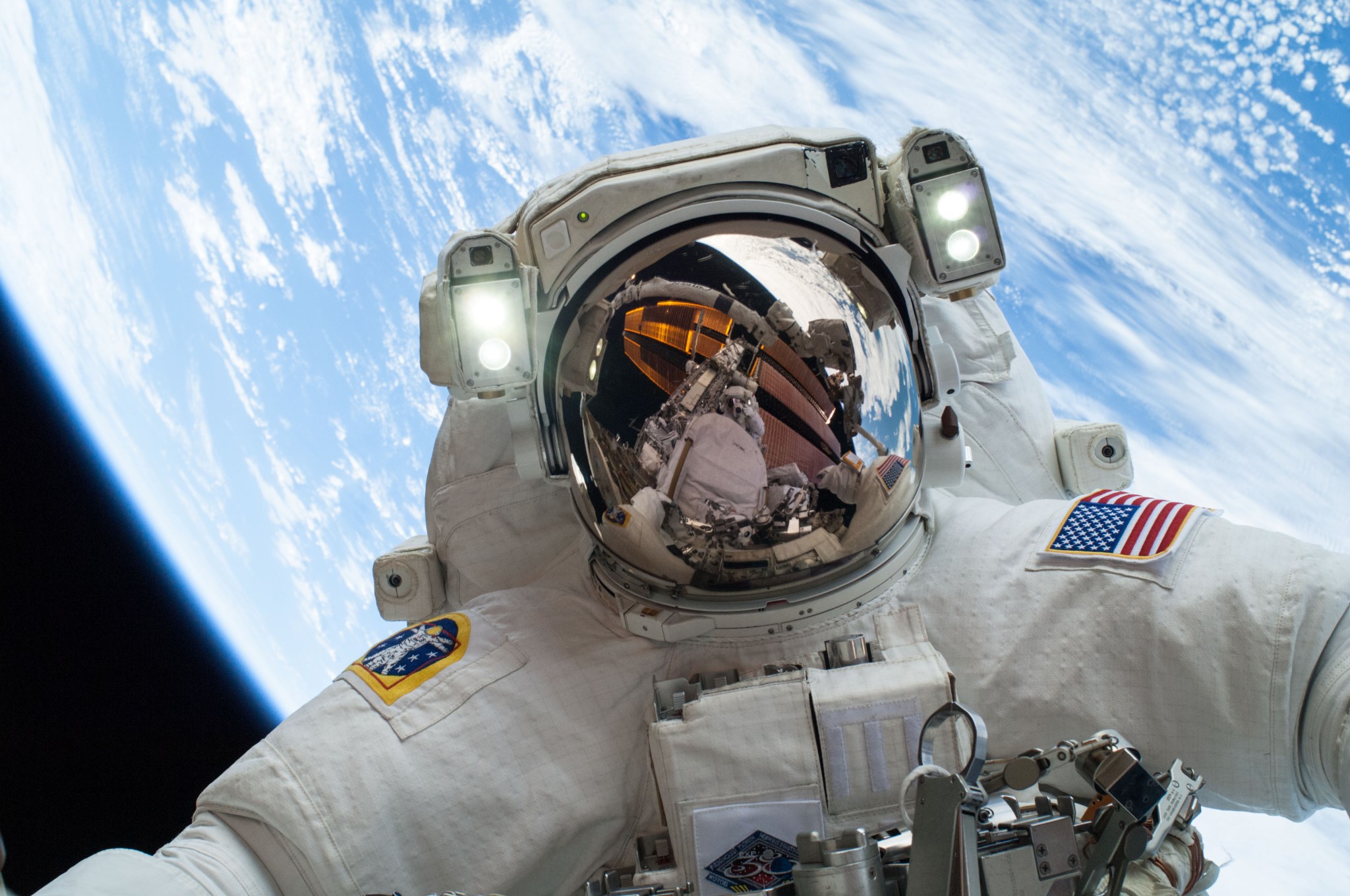 NASA astronaut Mike Hopkins on a spacewalk with International Space Station and fellow spacewalker visible in helmet visor