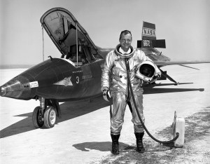 Black and white photo of Bill Dana, a NASA research pilot holding his helmet standing next to the X-15 aircraft.