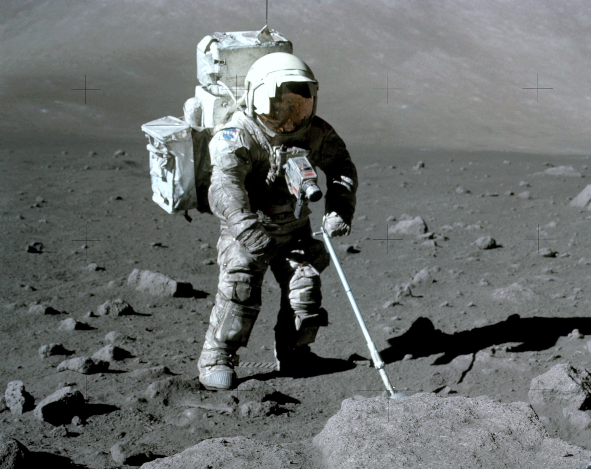 Apollo 17 lunar module pilot Harrison Schmitt uses an adjustable sampling scoop to retrieve lunar samples during the second Apollo 17 moon walk. His spacesuit is covered with a layer of the lunar dust.