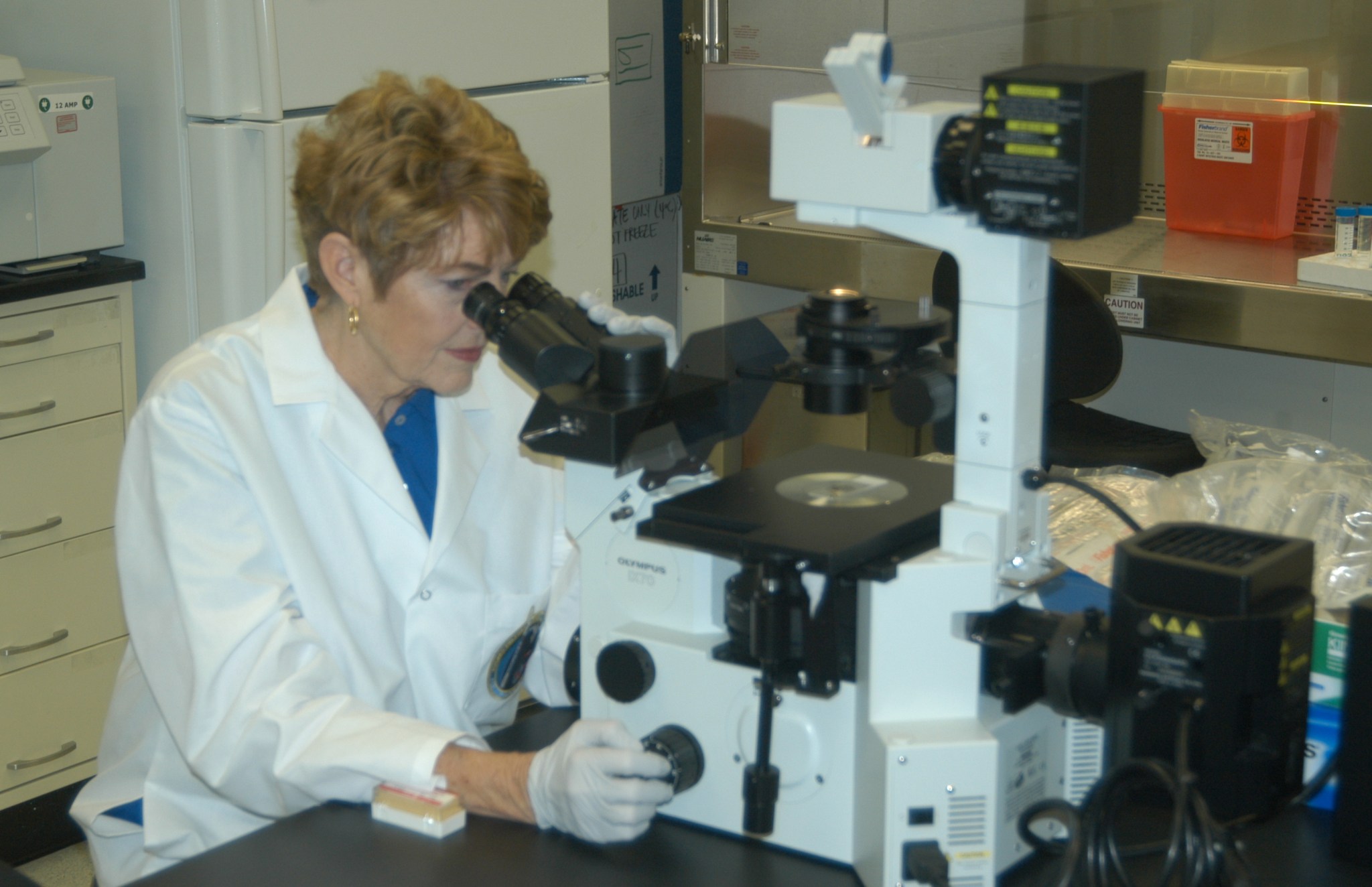 A woman in a white lab coat looks into a microscope