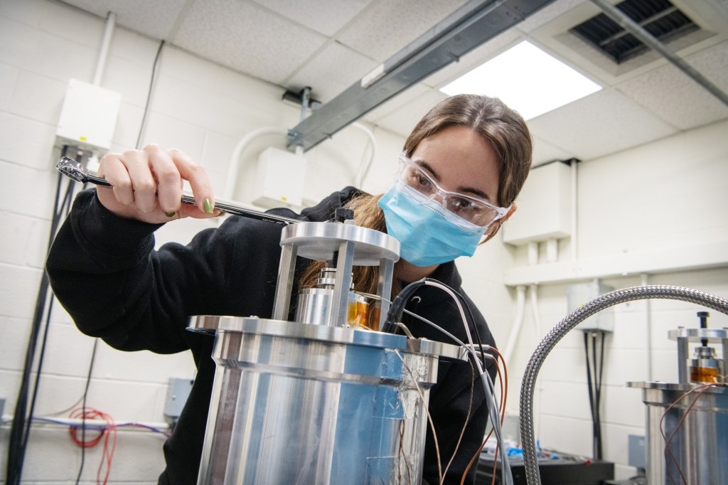 Masked female researcher behind a Stirling converter taking a measurement.