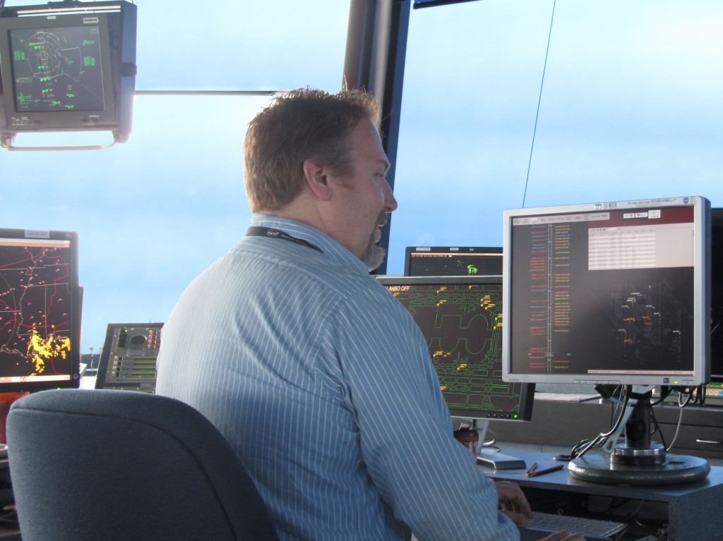 A man sitting at a desk in an air traffic control tower looking at a monitor.