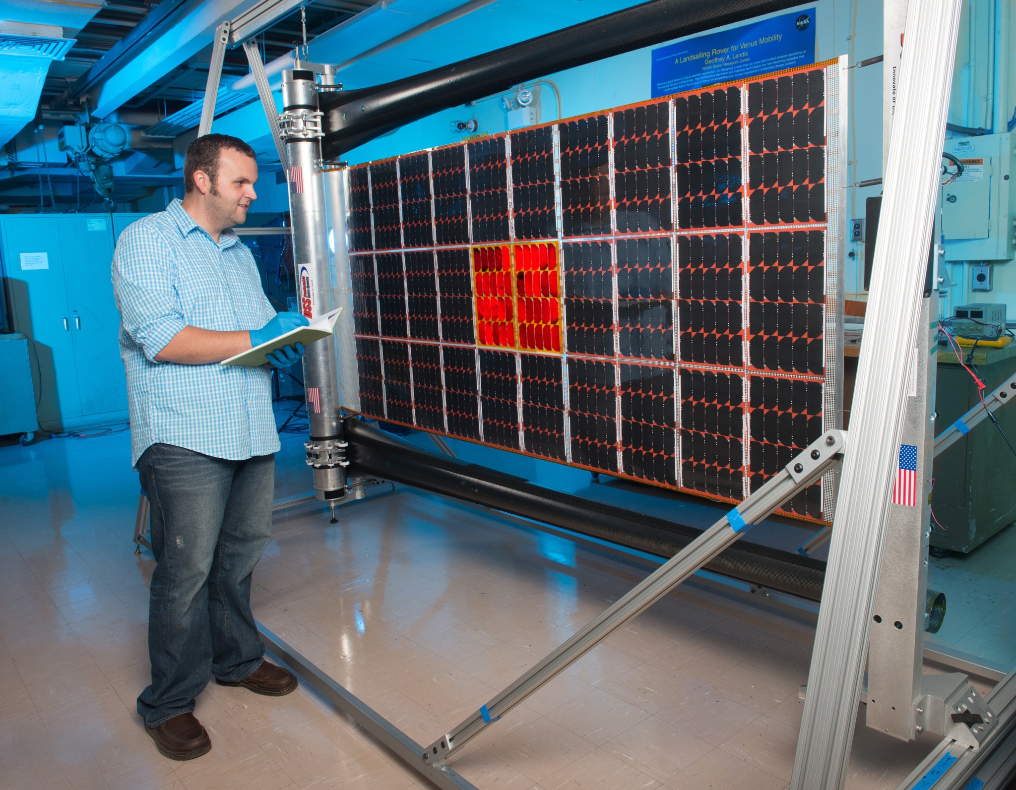 A man wears gloves and makes notes in a notebook while examining a solar cell in a lab at NASA Glenn