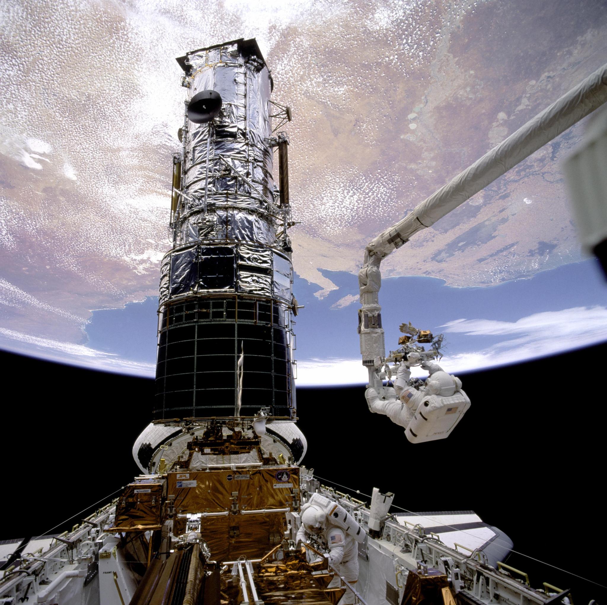 Astronaut on spacewalk outside space shuttle working on Hubble telescope.