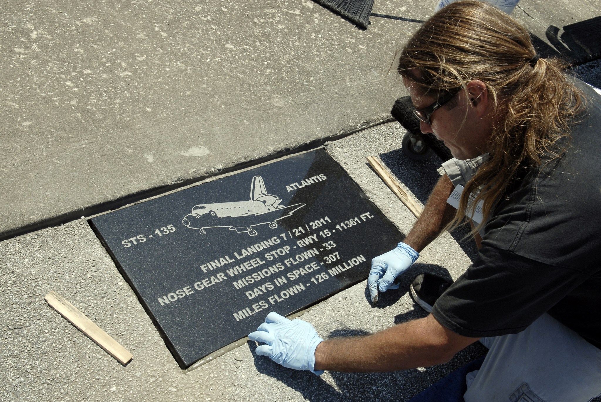 Man with gloved hands installing black stone plaque with shuttle image and text