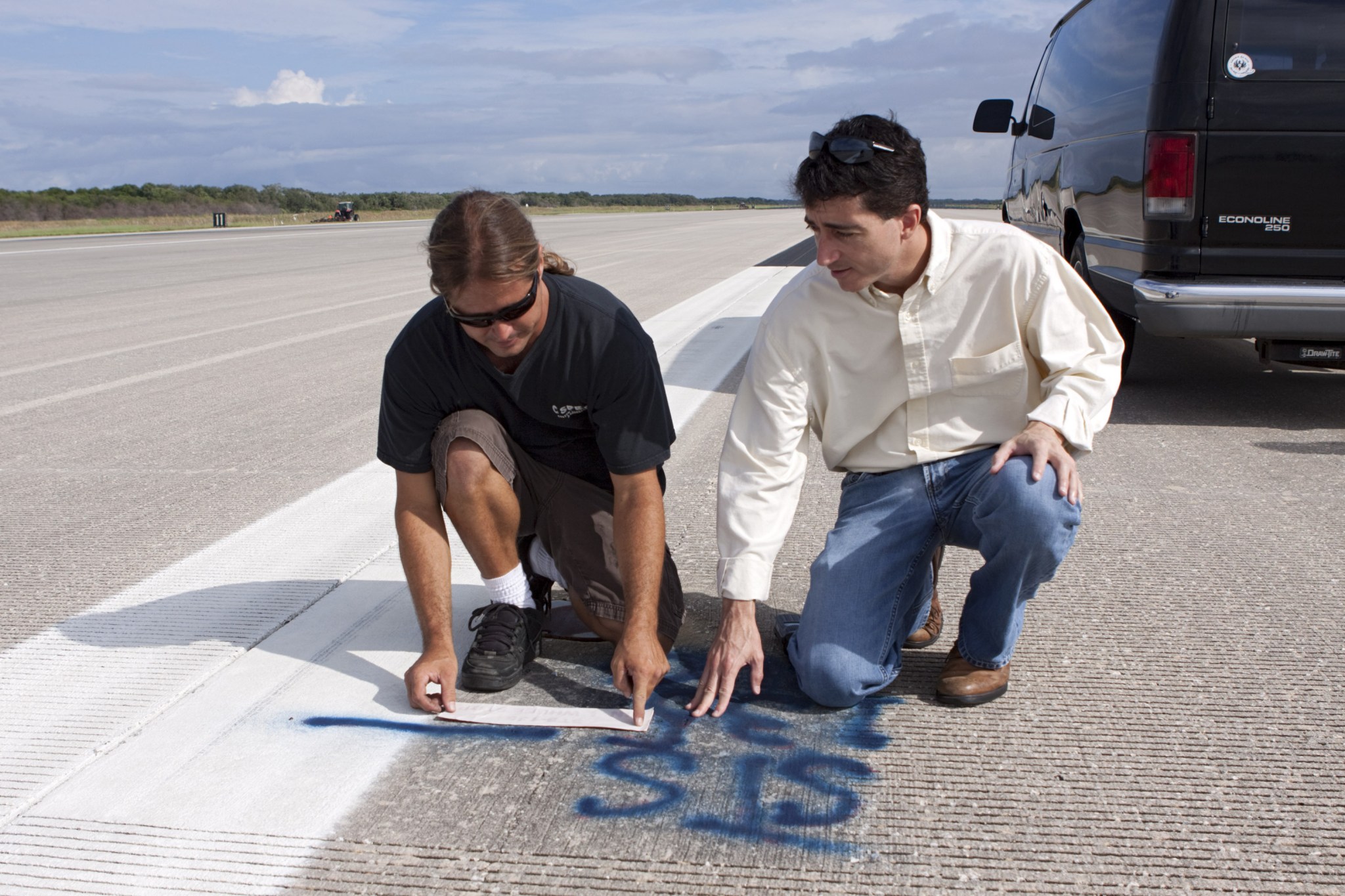 Two men marking pavement with paint where shuttle wheels stopped