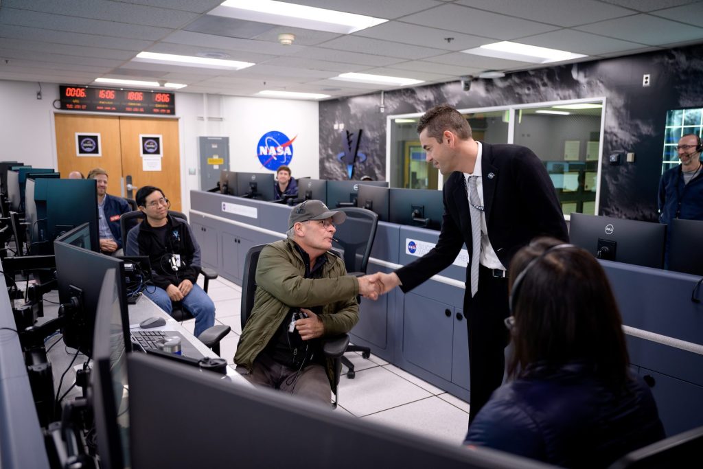 a group of people sitting at desks with computers and one is shaking the hand of a man standing