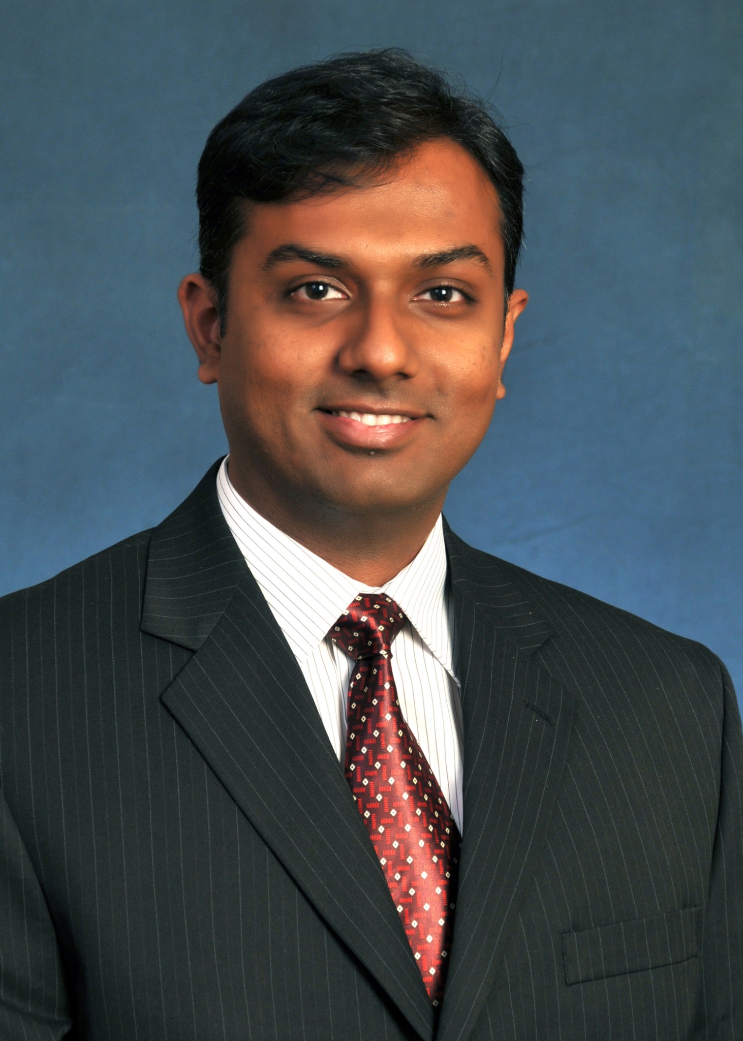 Vijay Chandrasekharan wearing a dark suit against a blue background.