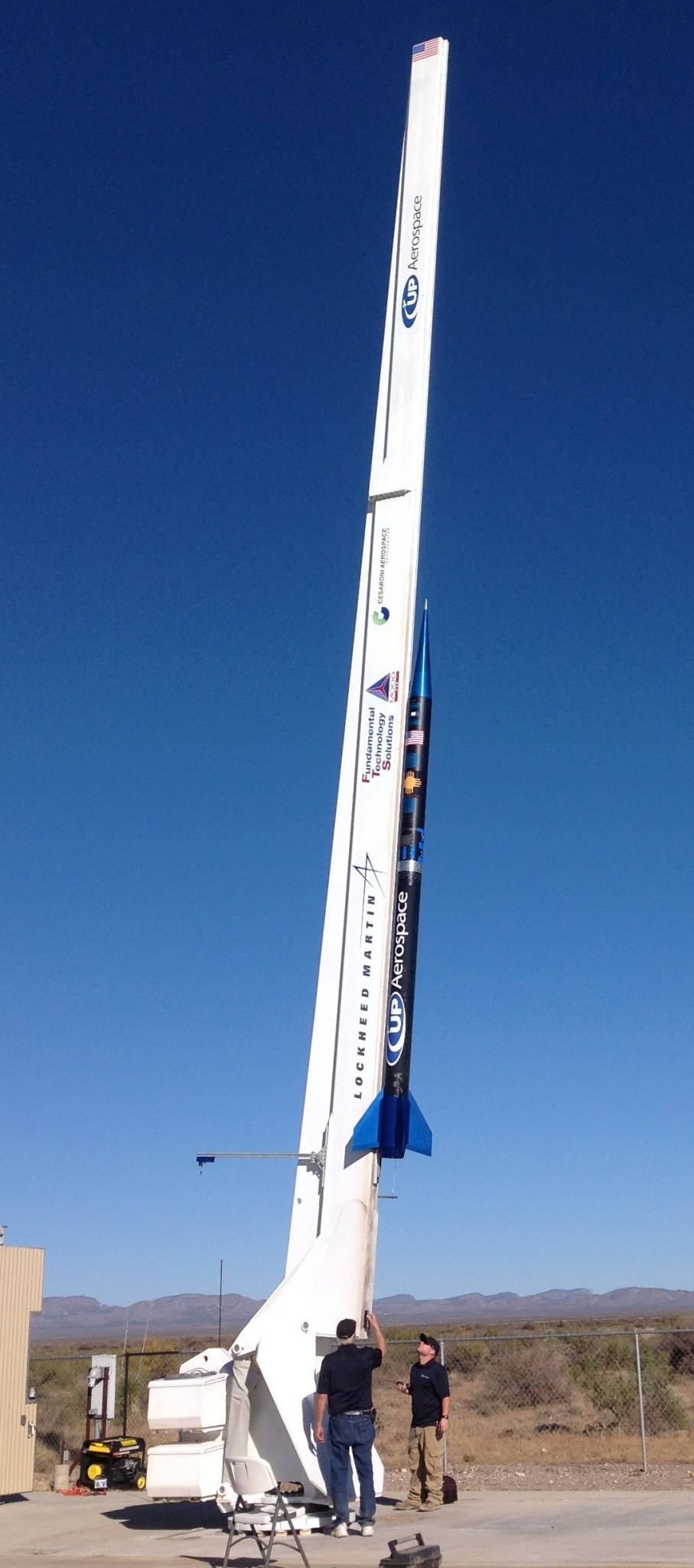 Two technicians stand beneath sounding rocket pointing toward the sky.
