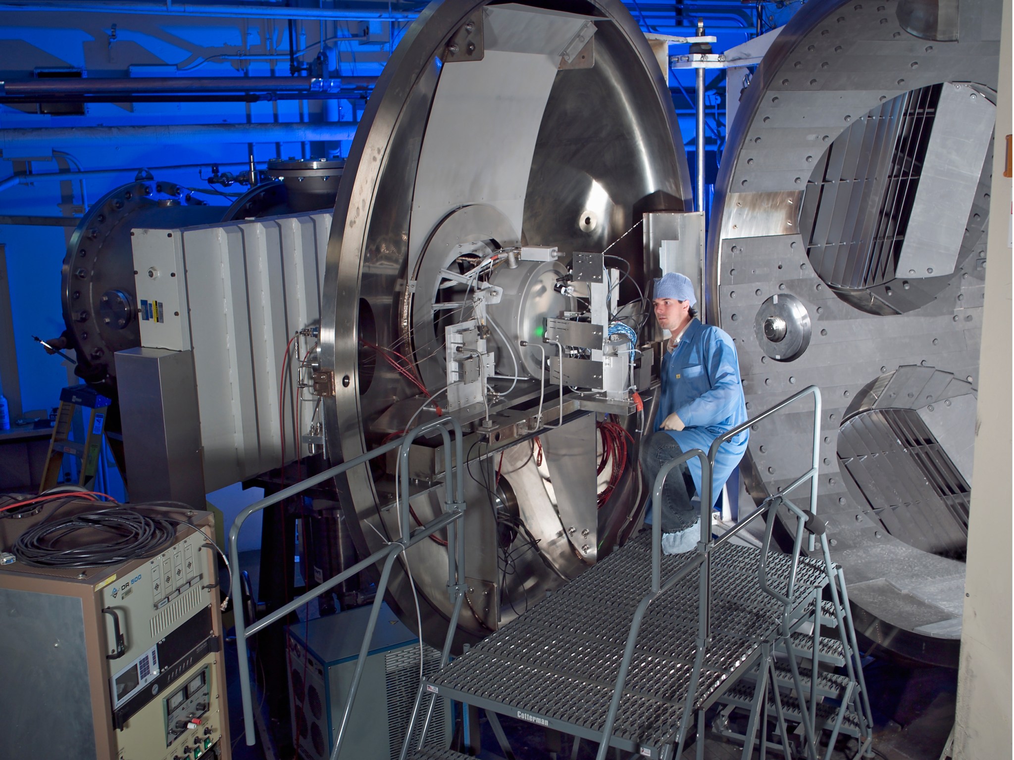 a researcher wearing a cleansuit, stands on a metal staircase to view a test article.